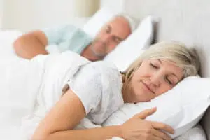 A woman and man sleeping in bed with pillows.